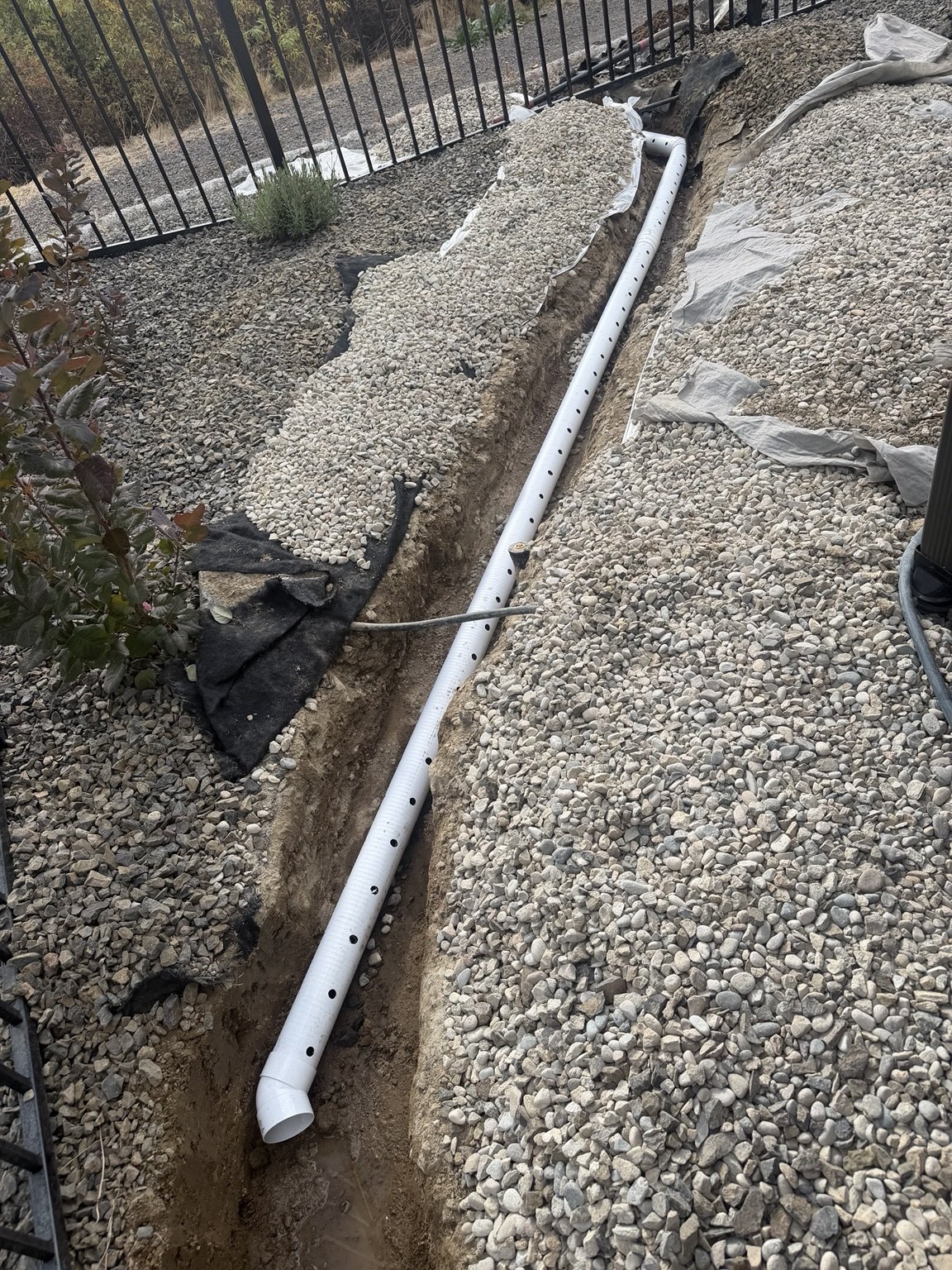 French drain pipe installation through a gravel landscape bed
